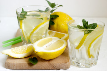 Lemonade with lemon slices, mint and ice and lemons on a light concrete background. Rustic style.