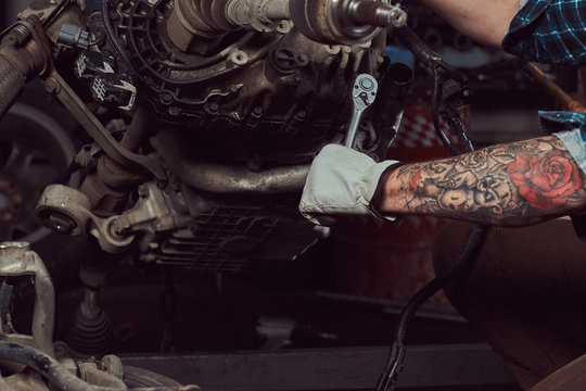 Close-up image of a tattooed mechanic specialist repairs the car engine with a wrench in the garage.