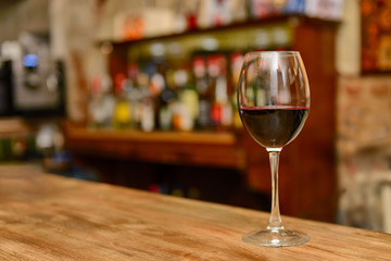 Glass of red wine on the bar counter with bottles in blurred background