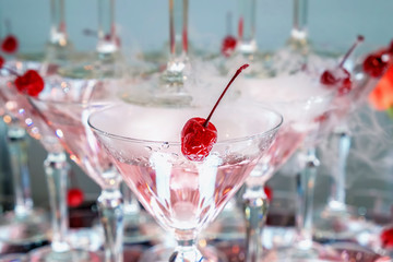 Red cocktail cherry in a glass with a pink alcoholic drink. Closeup view.
