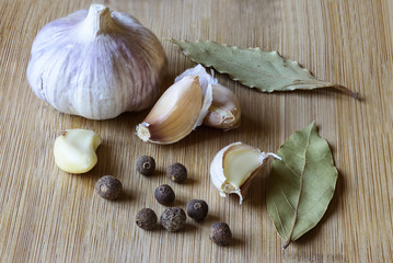 Garlic slices, small pepper and bay leaf on a wooden background