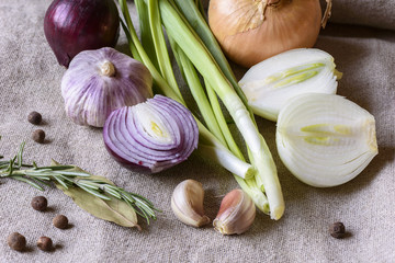 Garlic slices, halves of onions, rosemary on sackcloth texture background