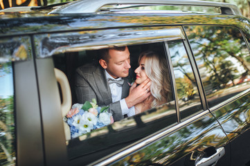 Beautiful newlyweds in a car window. The bridegroom embraces a sweet bride with curly hair. Portrait of stylish newlyweds.