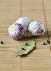 Three bulbs of garlic, bay leaf and black pepper on a mat