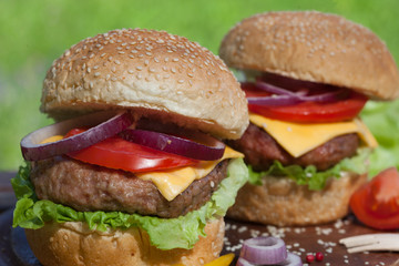 Close up of two fresh burgers with cheese and vegetables.