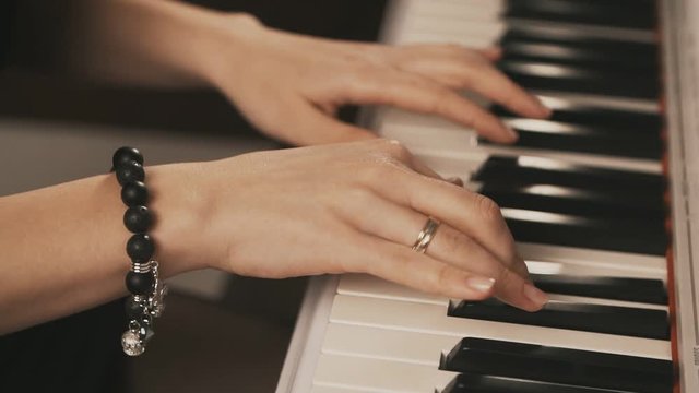 Female hands playing piano. Female hands with bracelet on piano. Woman touches fingers on keys. Close up.