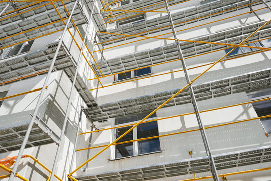 scaffolding near a new house, building exterior, construction and repair industry, white wall and window, yellow pipe