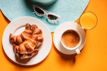 hat, sunglasses croissant with a cup of coffee and a glass of orange juice on a yellow table in the sun