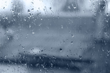 Raindrops on glass against blurred houses, a symbol of rain and mood