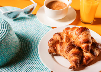 hat, sunglasses croissant with a cup of coffee and a glass of orange juice on a yellow table in the sun