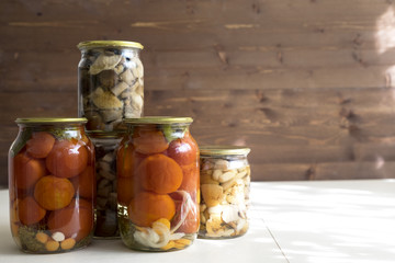 Marinated cucumbers, tomatoes and mushrooms in glass jars on the table.