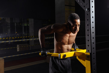 fitness, sport, bodybuilding and people concept - young athletic african american man doing triceps dip exercise on parallel bars in gym