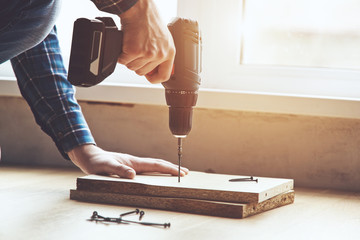 mans hands working with electric screwdriver and wooden plank