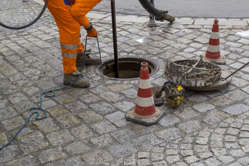 sewerage worker on street cleaning pipe