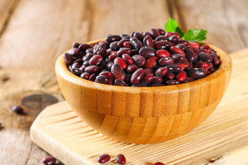 Red raw beans with greens on a wooden table.