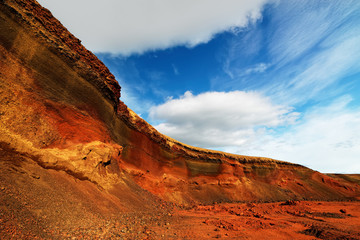 Colorful deposits of volcanic ash in reds and yellows against a green hill, above blue sky with clouds - Location: Iceland, Golden Circle