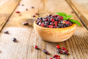 Red raw beans with greens on a wooden table.