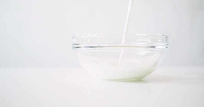 Milk is poured into a transparent glass bowl. White clear background with beverage.