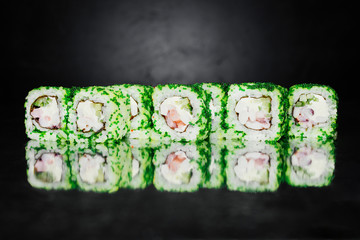 Sushi roll on dark background made of Nori, Marinated rice, Tobacco green caviar, Philadelphia Cheese, Cucumber, Sea Cocktail. Sushi menu. Japanese food. Free-space. Close-up.