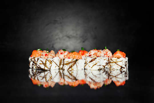Sushi roll tobica on dark background made of nori, marinated rice, cheese, cucumber, avocado, salmon tartar, tartar from perch, spicy sauce, massago. Sushi menu. Japanese food. Free-space