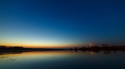 Sky with the stars before dawn. Night landscape with a lake.