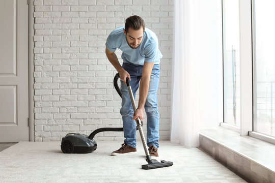 Young man cleaning carpet with vacuum at home