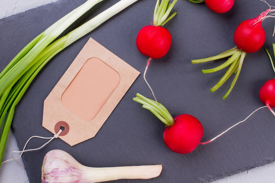 Red salad radish and paper tag. Young garlic, onion and radish on slate board. Organic vegetable gardening.