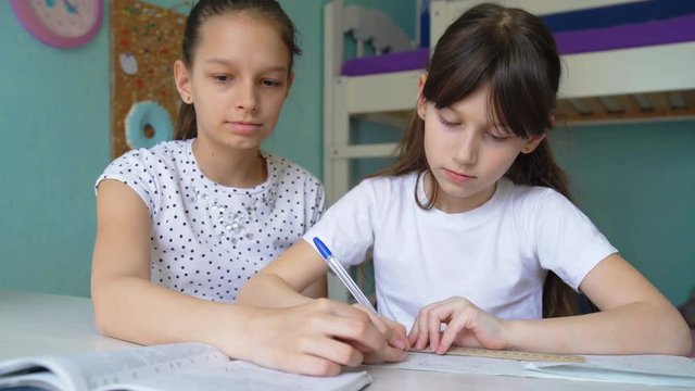 two caucasian girls doing homework discussing lessons. pupils studying at home. one girl helping another