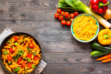 Italian penne pasta in tomato sauce and different type of vegetables, on a wooden background