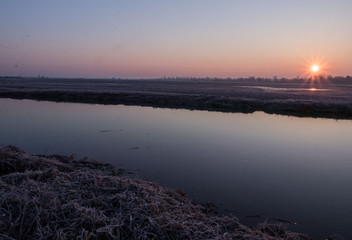 sunrise on the background of a winding wild river, its backwaters and backlit with reed promises, early spring