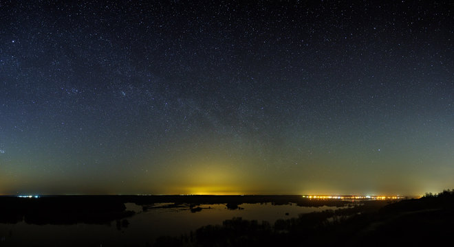 The stars of the Milky Way in the sky before dawn. Night landscape with a lake. Panoramic view of the starry space.