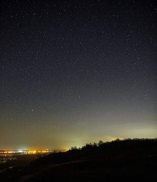 Starry sky at night over the city and forest. Landscape with a long exposure.