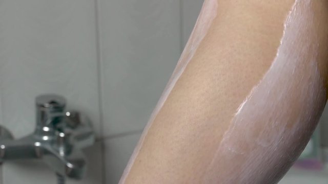 Young Woman Shaves Slim Legs With Hair Removal Cream in Bath.
