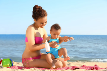 Young African American mother and daughter with suntan lotion on beach at resort