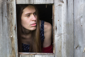Young woman with long hair looks out of the wooden shed windows.