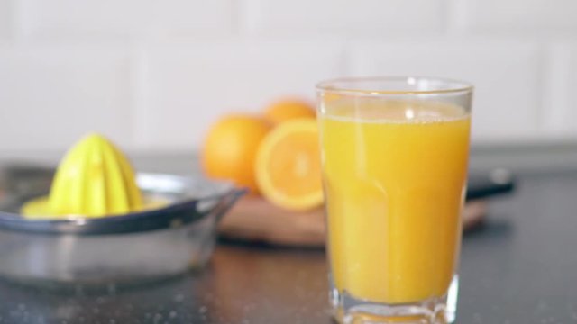 Slow motion a young woman is doing morning for her family a fresh orange juice in the kitchen in the house. Hand squeezes juice from organic oranges on a juicer to pour the juice into a glass beaker
