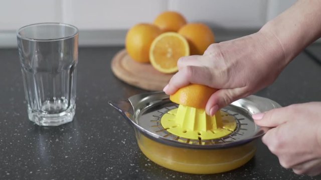 Slow motion a young woman is doing morning for her family a fresh orange juice in the kitchen in the house. Hand squeezes juice from organic oranges on a juicer to pour the juice into a glass beaker