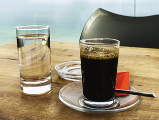 Strong and dark coffee in a glass served with a glass of water on a wooden table 