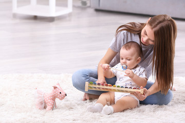 Young mother and cute baby playing on floor at home