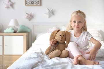 Cute little girl hugging toy bunny on bed at home