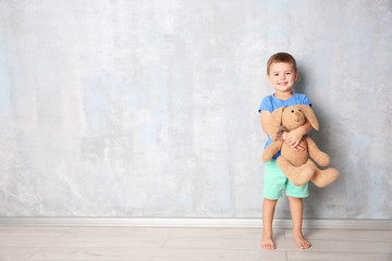 Cute little boy with toy bunny near grey wall