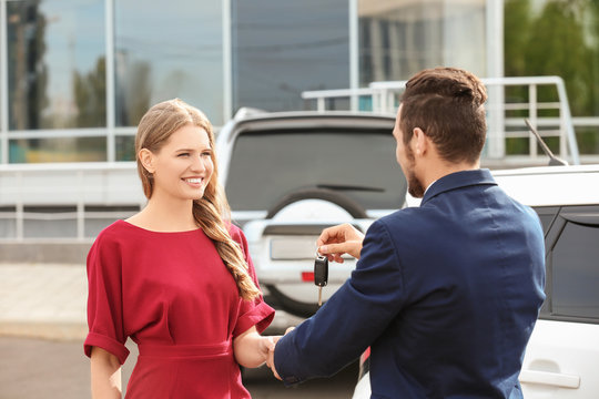 Salesman giving car key to customer outdoors