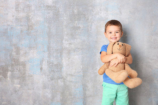 Cute little boy with toy bunny on grey background
