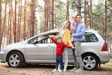 Young couple with their little children near car in pine forest