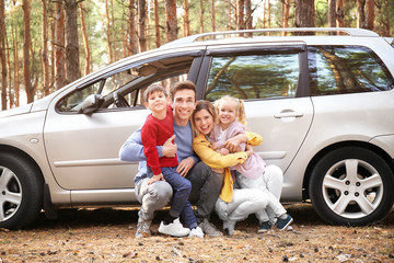 Young couple with their little children near car in pine forest