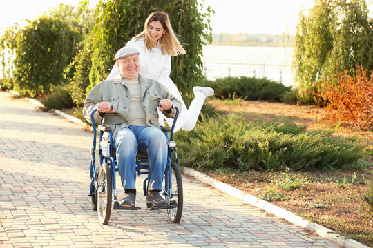 Nurse from care home and senior man in wheelchair walking outdoors