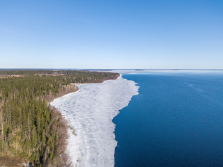 Fototapeta na wymiar Aerial view of the shoreline of the lake and pieces of melting ice along the shore