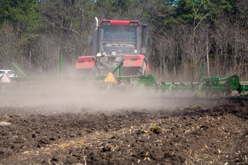 Fototapeta premium Rolnik w ciągniku przygotowuje ziemię z kultywatorem przedsiewnym