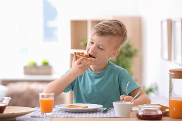 Cute little boy eating tasty toasted bread with jam at table © New Africa