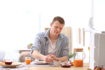 Young man spreading jam onto tasty toasted bread at table